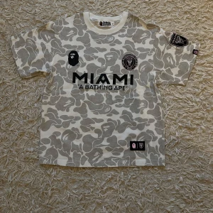 Bape x Inter Miami fotbollströja- med originella lappar - Helt ny, aldrig använd och med originaletiketterna kvar! Denna unika BAPE x Inter Miami fotbollströja i mjuk bomull kombinerar streetwear och fotboll på ett stilrent sätt som få andra plagg kan. Perfekt för dig som vill sticka ut i sommar med ett exklusivt och bekvämt plagg. Missa inte chansen att lägga vantarna på denna eftertraktade tröja!  Hör av dig direkt vid minsta intresse!