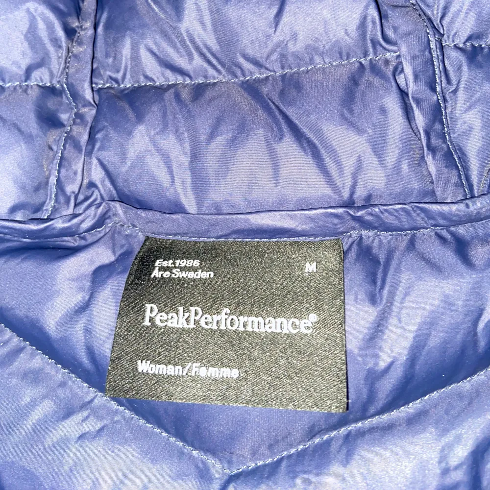 Säljer en snygg blå dunjacka från Peak Performance. Jackan har en praktisk huva och dragkedja framtill. Perfekt för kyliga dagar med sin quiltade design som håller värmen.. Takit.