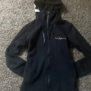 Svart jacka från Peak Performance - Snygg svart jacka från Peak Performance med dragkedja och huva. Perfekt för kyligare dagar med sin stilrena design och bekväma passform.