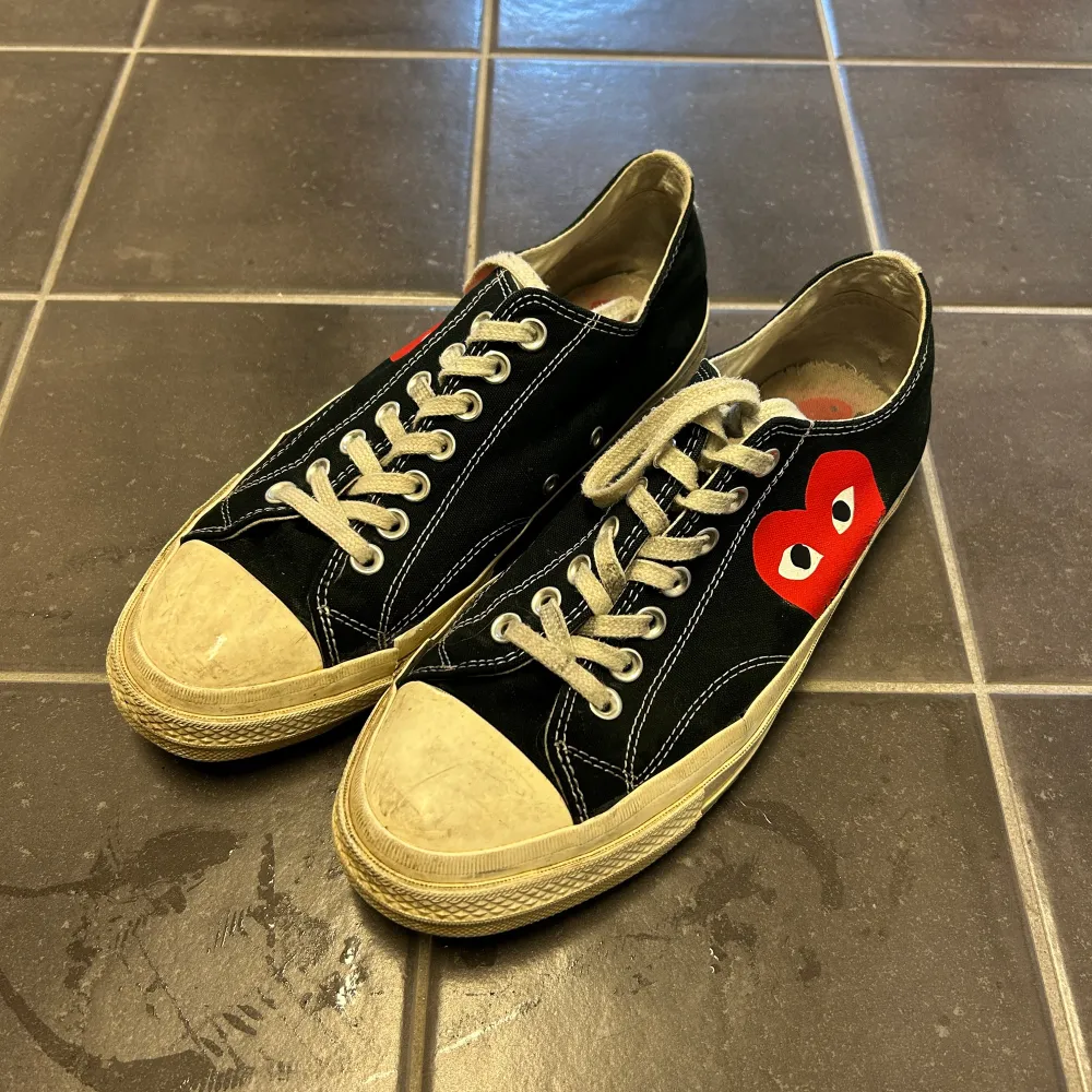 Säljer ett par svarta Converse sneakers med en röd hjärtdetalj på sidan. Skorna har vita snören och en klassisk gummisula. Perfekta för en avslappnad stil.. Kengät.