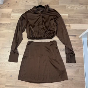 Brunt set från Nelly x Bianca - Snygg brun kjol från Nelly x Bianca i ett set med matchande skjorta. Kjolen har en enkel design med en rak passform och är tillverkad i ett glansigt material. Perfekt för en stilren look.