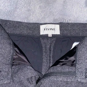 Grå byxor från Elvine - Snygga grå byxor från Elvine i en klassisk stil. Byxorna har en dragkedja och knappar framtill samt fickor på sidorna. Perfekta för en stilren look. Jag har 32 i längd och den passar mig bra.