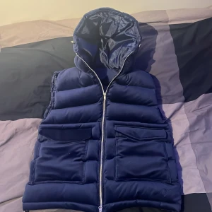 Mörkblå manchester väst med huva - Snygg mörkblå Manchester västmed dragkedja och praktiska fickor. Västen har en mysig huva och är perfekt för kyligare dagar. Aldrig använd säljer för att den kom aldrig till användning . Ny pris 999 mitt pris 749kr. Storlek M. ! Inga byten!