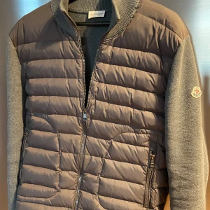 Moncler cardigan jacka - Snygg grå cardigan jacka från Moncler med dragkedja och snygga detaljer. Jackan har långa ärmar och en stilren design som passar perfekt för kyligare dagar. Storlek 2/S-M