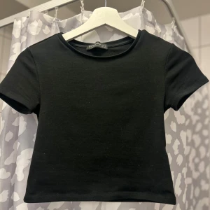 Svart croppad t-shirt - Snygg svart croppad t-shirt med korta ärmar. Perfekt för en avslappnad stil. Enkel och stilren design som passar till det mesta.