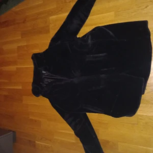 Svart pälsjacka - Snygg och elegant svart pälsjacka med långärmad design. Perfekt för kyligare dagar med sin mjuka och lyxiga känsla. Jackan har en klassisk passform och är ett stilrent tillskott till garderoben.