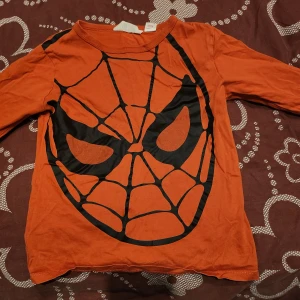 Orange långärmad tröja med spindelmotiv - Cool orangeröd långärmad tröja med ett stort svart spindelmotiv på framsidan. Perfekt för fans av superhjältar och en färgklick i garderoben.