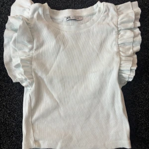 Vit ribbad topp från Zara - Säljer en söt vit ribbad topp från Zara med volangdetaljer på ärmarna. Säljs inte längre 