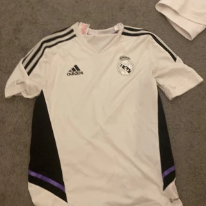 Vit Real Madrid fotbollströja från Adidas - Säljer en snygg real Madrid träningströja från 22/23 säsongen, skicket är väldigt bra då den inte har använts så mycket, den är köpt från unisport för cirka 500kr, hör av er om ni har några funderingar