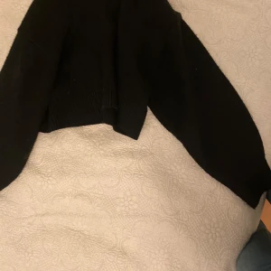 Svart stickad tröja - Säljer en svart stickad tröja med hög krage och långa ärmar. Tröjan har en croppad passform som ger en modern look. Perfekt för kyligare dagar.