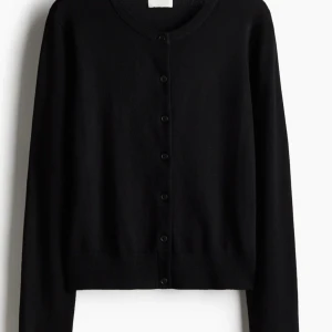 Svart kofta med knappar - Snygg och stilren svart kofta med knappar framtill. Perfekt för lager-på-lager och passar till många olika outfits. Långärmad design med rund halsringning. Storlek 158 