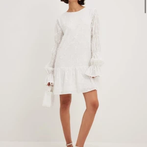 Vit broderad klänning - Oanvänd med lappen kvar! Charmig vit klänning med broderade blommor och volangdetaljer. Den har långa ärmar med elastiska avslut och en lös passform som ger en luftig känsla. Perfekt för sommarens festligheter eller en student. Sitter väldigt bra i längden. Första bilden är lånad från hemsidan (original pris 799kr). Storlek 38, passar som S/M