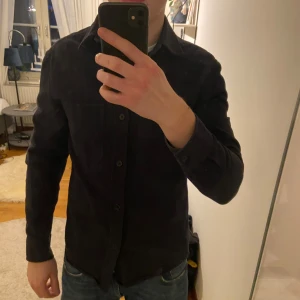 Mörkblå skjorta  - Snygg svart skjorta från H&M med klassisk krage och knappar framtill. Perfekt för en stilren look. Skjortan har långa ärmar och en normal passform. Använt kanske 4 gånger men som ny den är i storlek s men passar som m