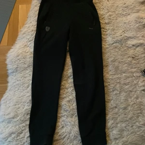 Svarta mjukisbyxor från Puma - Säljer ett par svarta mjukisbyxor från Puma med dragkedja på fickorna och Ferrari logga.Perfekta för en avslappnad stil eller träning. Byxorna har en normal passform och är tillverkade i ett mjukt material för extra komfort.