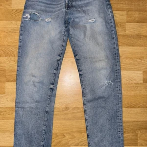 Blå slitna jeans - Säljer ett par blå ZARA  jeans med slitningar och fransiga kanter. De har en klassisk femficksdesign och en straight passform. Perfekta för en avslappnad stil.