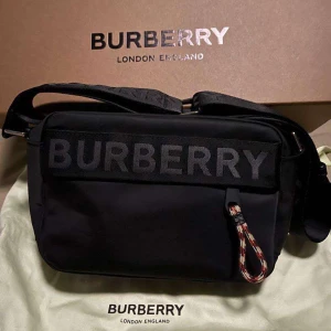 Burberry axelväska  - Burrberry axelväska: felfri använd endast en sommar, går att även ändra storleken på bandet på hur man vill att den ska sitta. Priset går att diskutera! loggan står på  väskan och bandet samt färgerna på dragkedjan på nedre fickan. Jag har personligt tagit bilden när jag köpte den för flera bilar kontakta privat! 