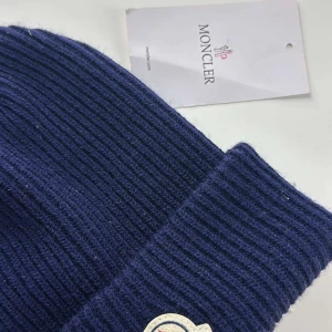 Mörkblå ribbad mössa från Moncler - Snygg och stilren mörkblå mössa från Moncler med ribbad design. Perfekt för kyliga dagar. Mössan har Monclers logotyp framtill och en etikett på sidan.