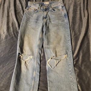 Blå jeans med slitningar från Perfect Jeans - Säljer ett par blå jeans från Perfect Jeans med coola slitningar på knäna. De har en klassisk femficksdesign och en bekväm passform. Perfekta för en avslappnad stil.