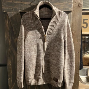 Stickad tröja - Tjaba, säljer en fin, knappt använd beige stickad tröja i strl L då jag inte använder den längre. Den är stickad i annat mönster på kragen å längst ner vid armarna vilket är fina detaljer. Den sitter som en L ska göra och den väger lite precis som en sån här stickad tröja ska göra. Dragkedjan är inte i plats vilket är bra och den har en liten läderlapp som man drar i vilket är en kvalitets detalj. Priset är redan väldigt rimligt då den aldrig använts men helt hugget i sten är det inte🙏