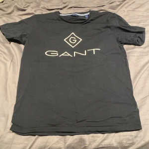Svart t-shirt från GANT - Snygg svart t-shirt från GANT med stort tryck på framsidan. Perfekt för en avslappnad stil. Tillverkad i mjukt material för extra komfort.