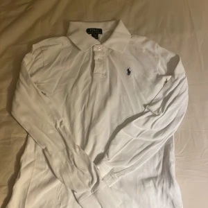 Vit långärmad pikétröja från Ralph Lauren - Säljer en klassisk vit långärmad pikétröja från Ralph Lauren med den ikoniska loggan broderad på bröstet. Tröjan har en stilren krage och knappar framtill. Är igentöigen inte skrynklig är bara nytvättad pris kan diskuteras 