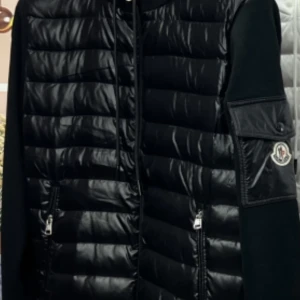 Svart dunjacka från Moncler - Snygg svart dunjacka från Moncler med quiltad design och dragkedja. Jackan har en praktisk ficka på ärmen och är perfekt för kyligare väder.