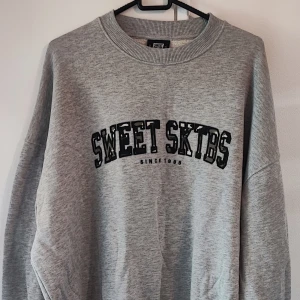 Grå sweatshirt från Sweet SKTBS - Säljer en grå sweatshirt från Sweet SKTBS med tryck framtill. Tröjan har en rund halsringning och långa ärmar, perfekt för en avslappnad stil. Passar bra till både jeans och joggers. Storleken är S men passar till M också.