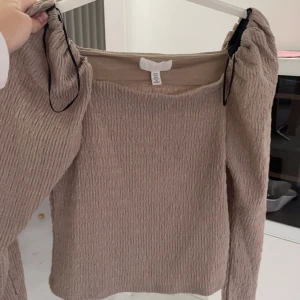 Beige ribbad topp från H&M - Säljer en stilren beige ribbad topp från H&M. Toppen har långa ärmar och en fyrkantig halsringning. Perfekt för en avslappnad men chic look.