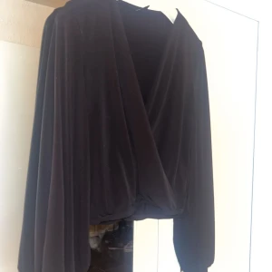 Svart omlotttröja från Gina Tricot - Elegant svart omlotttröja från Gina Tricot med långa ärmar och en djup v-ringning, Den är stretchig och lös/ luftig. Använt ett par gånger