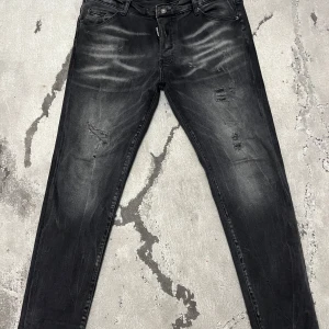 Svarta jeans från Dsquared2 - Snygga svarta jeans från Dsquared2 med slitna detaljer och en cool tvättad look. De har en klassisk femficksdesign och knappgylf. Perfekta för en trendig stil. Byxorna är storlek 56 och om ni vill ha några mer bilder eller om ni har några frågor är det bara att skriva