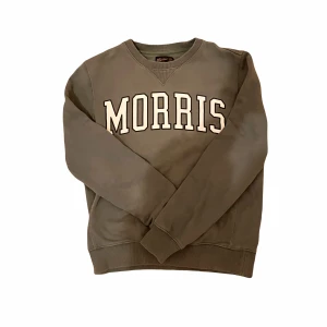 Grön sweatshirt från Morris - Säljer en stilren grå sweatshirt från Morris med deras logga i vitt på bröstet. Tröjan har långa ärmar och ribbade muddar vid ärmslut och nederkant. Perfekt för en avslappnad stil.