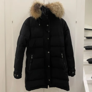 Svart dunjacka/vinterjacka med päls från Hollies - Säljer en stilren svart dunjacka/vinterjacka från Hollies med en äkta lyxig pälsdetalj på huvan. Jackan har långa ärmar och praktiska dragkedjor på fickorna. Perfekt för kalla vinterdagar. Avtagbar päls. Pris kan även diskuteras :) 
