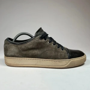 Lanvin Captoe - Snygga grå sneakers från lanvin i mocka med svarta snörningar och blanka svarta detaljer på tån. Skorna har en beige sula som ger en cool kontrast. Perfekta för en stilren look.