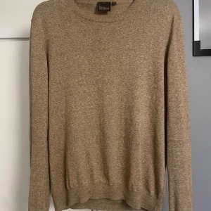 Beige tröja från Oscar Jacobson - Säljer en stilren beige tröja från Oscar Jacobson. Tröjan har en klassisk rund hals och långa ärmar, perfekt för en elegant och avslappnad look. Passar bra till både vardag och mer uppklädda tillfällen.