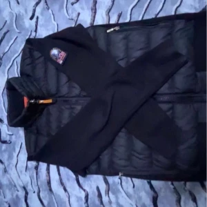 Svart dunväst från Parajumpers - Säljer en svart dunväst från Parajumpers med dragkedja och en snygg logga på bröstet. Perfekt för kyliga dagar när du vill hålla stilen. Västen har en klassisk design och är lätt att matcha med olika outfits.