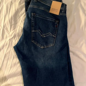 Mörkblå jeans från Replay - Snygga mörkblå Replay Hyperflex jeans i modellen Grover. De har en straight passform och klassisk femficksdesign med dragkedja. Perfekta för en stilren look. Storlek W32 L32