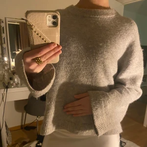 Grå stickad tröja - Mysig grå stickad tröja med rund hals och långa ärmar. Perfekt för kyliga dagar med sin mjuka och bekväma passform. Ribbstickade muddar vid ärmslut och nederkant ger en stilren look.