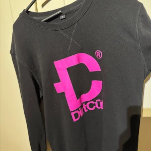 Svart tröja med rosa tryck från Dirtcult - Säljer en svart långärmad tröja från Dirtcult med ett stort rosa tryck på framsidan. Storleken är i S och är i bra skick och använd fåtal gånger.