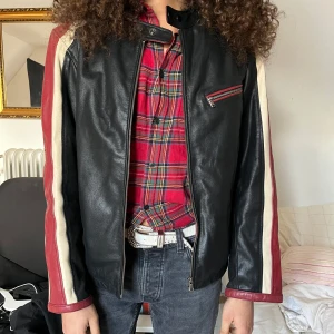 Svart skinnjacka med röda och vita detaljer - supersnygg köpt på second hand men används tyvärr inte :( märkt storlek XL men gammal storlek, skulle uppskattas som en oversize M typ? 