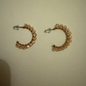 Rosa pärlade örhängen - Snygga örhängen i creol-stil med rosa pärlor. De har en elegant design med pärlor som är fästa runt en guldfärgad båge. Perfekta för att ge en glittrig touch till din outfit.