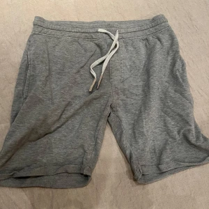 Grå shorts från Indicode Jeans - Säljer ett par grå shorts från Indicode Jeans. De har en bekväm passform med snörning i midjan och en bakficka med knappdetalj. Perfekta för en avslappnad stil.