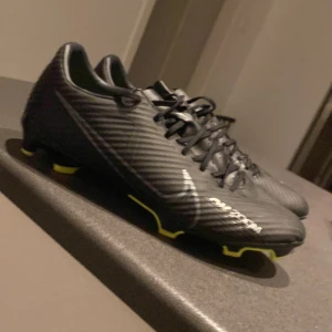 Svarta fotbollsskor från Nike - Snygga svarta fotbollsskor från Nike med limedetaljer och snörning. Modellen på skorna är Nike Mercurial Zoom Vapor 15 academy