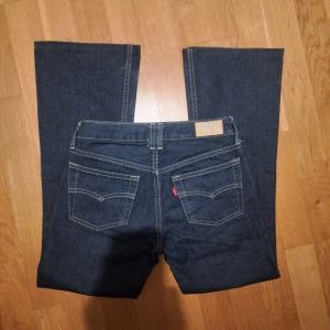 Mörkblå low waist bootcut jeans från Levis - Snygga mörkblå super low waist  bootcut jeans från Levis med klassisk femficksdesign och kontrastsömmar. Jeansen har en rak passform och är perfekta för en avslappnad stil. De har en knappgylf och bälteshällor.
