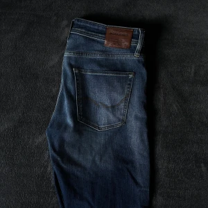 Mörkblå jeans från Jack & Jones - Snygga mörkblå jeans från Jack & Jones med klassisk femficksdesign och en läderpatch på baksidan. Modell på jeansen heter ”Tapered/Erik”. Kom privat vid funderingar