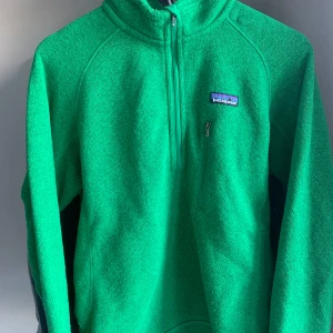 Patagonia Fleece - Säljer en grön fleece tröja från Patagonia med halv dragkedja och en praktisk bröstficka. Perfekt för kyliga dagar och utomhusaktiviteter. Tröjan har långa ärmar och en bekväm passform.
