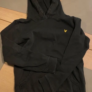 Svart hoodie Lyle & Scott - Säljer en svart hoodie med en liten broderad logga på bröstet. Tröjan har en klassisk design med huva och långa ärmar.  storlek 12/13 år. Kan hämtas i Skövde eller fraktas! Mvh Lukas.