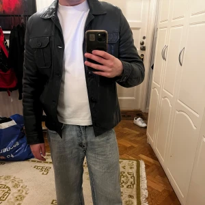 Mörkblå skinnjacka - Säljer en stilren mörkblå skinnjacka med knappar och två bröstfickor. Jackan har en quiltad insida för extra komfort och värme. Perfekt för en cool look när det är lite kyligare ute. Passar bra till jeans och sneakers. Bra skick, nypris ca 1500kr PM för fler frågor. Jag är 175