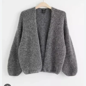 Grå stickad kofta - Mysig grå stickad kofta med en öppen design. Perfekt för kyliga dagar och ger en avslappnad look. Koftan har långa ärmar och en mjuk textur som känns skön mot huden.