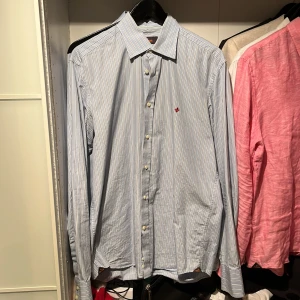 Morris skjorta - Snygg blå och vit randig skjorta från Morris med klassisk krage och knappar framtill. Perfekt för en stilren look. Perfekt nu till våren. motsvarar stl M. Nypris 1600kr 