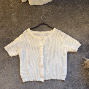 Vit stickad kofta - Säljer en söt vit stickad kofta med korta ärmar och knappar framtill. Perfekt för lager-på-lager och ger en mysig känsla. Passar bra till både jeans och kjol.